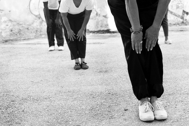 Black and white image of exercise group in a forward bend, with their hands on their knees.